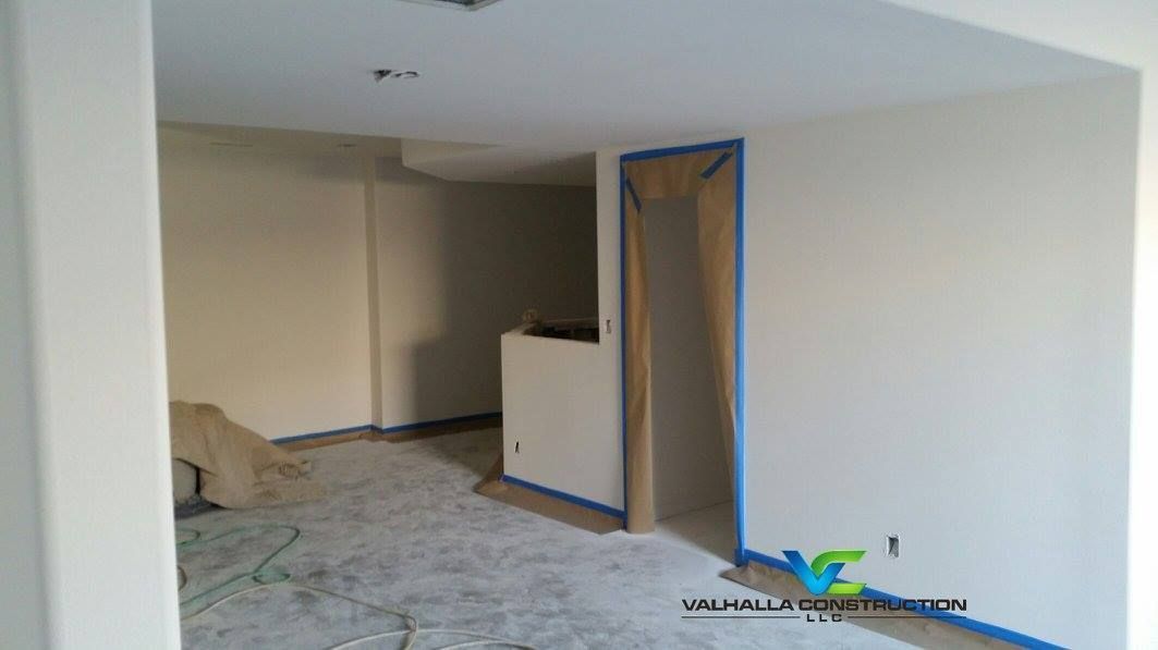 Interior room under renovation, light-colored walls, open doorway, blue tape, unfinished floor.