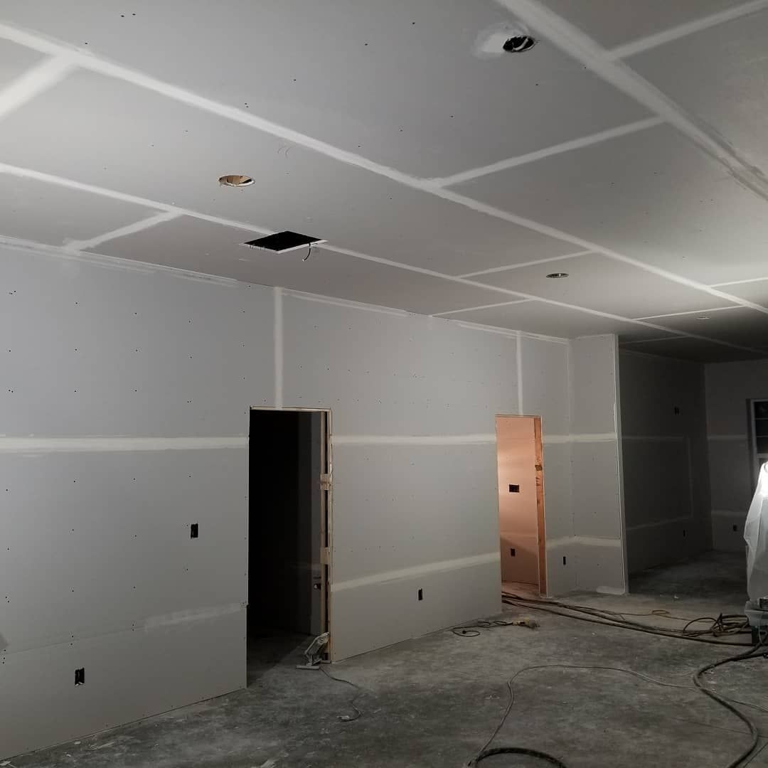 Interior of a room under construction with drywall on walls and ceiling, two doorways visible.