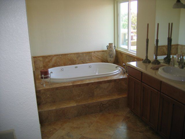 Bathroom with a raised marble-tiled jacuzzi tub, wooden vanity, and a window.