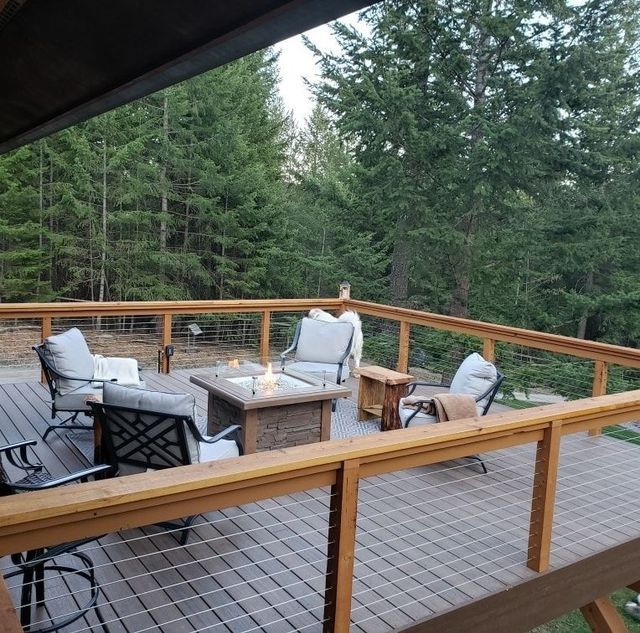 Outdoor deck with seating around a lit fire pit, trees in background.