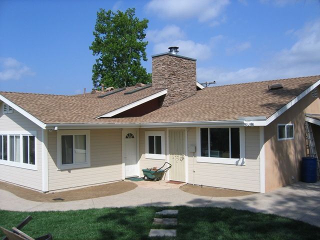 Beige house with a brown roof, chimney, and blue sky.