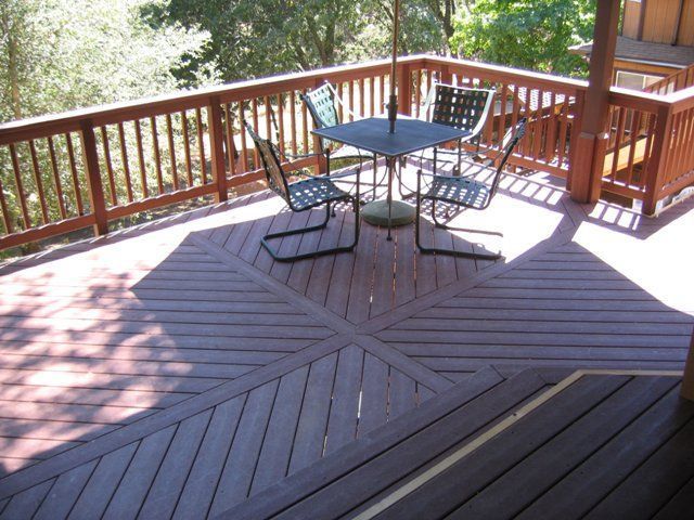 Wooden deck with a table, chairs, and umbrella. Patterned floor. Brown railing.