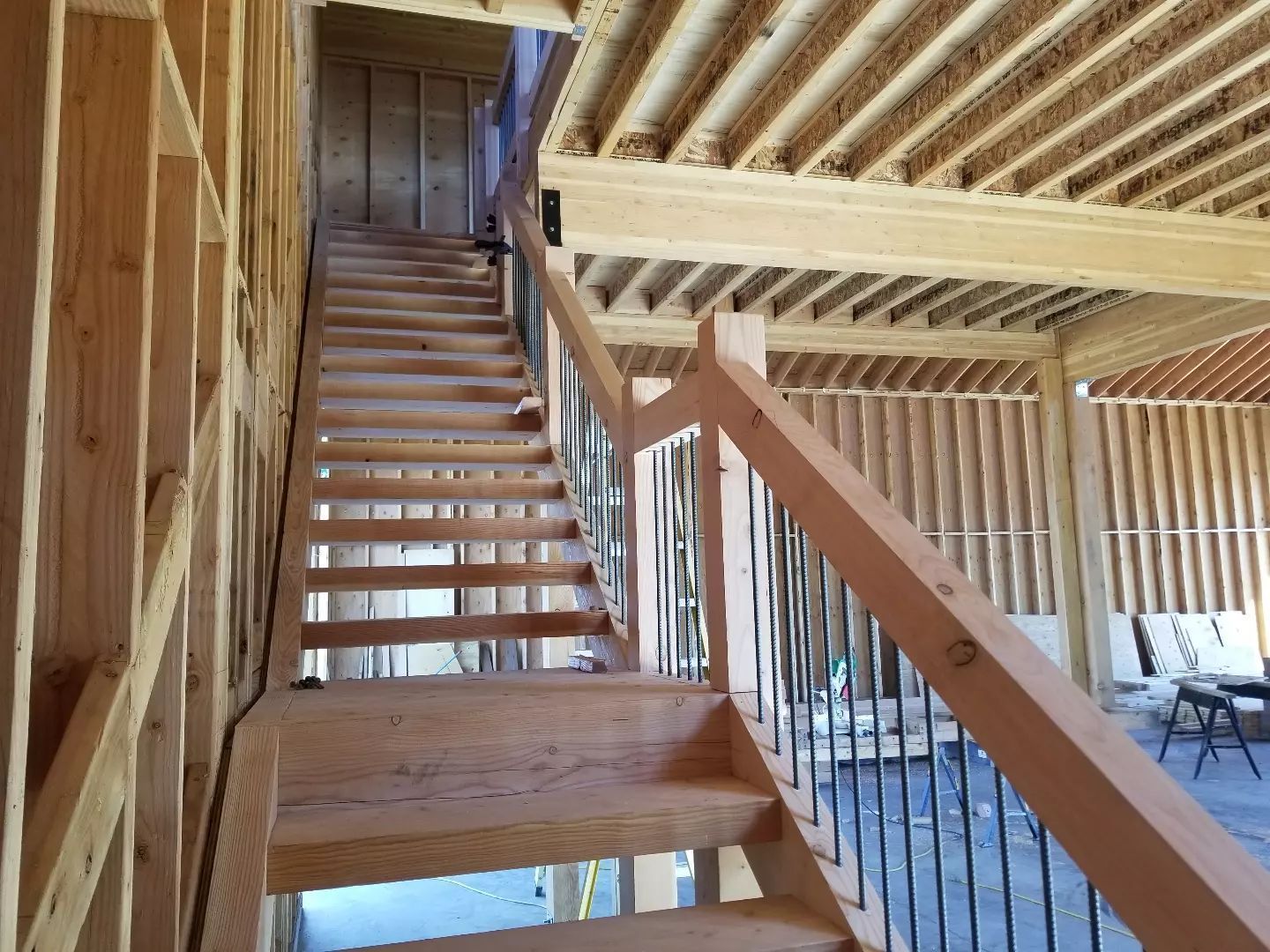 Wooden staircase in a building under construction, with open framing and metal railing.
