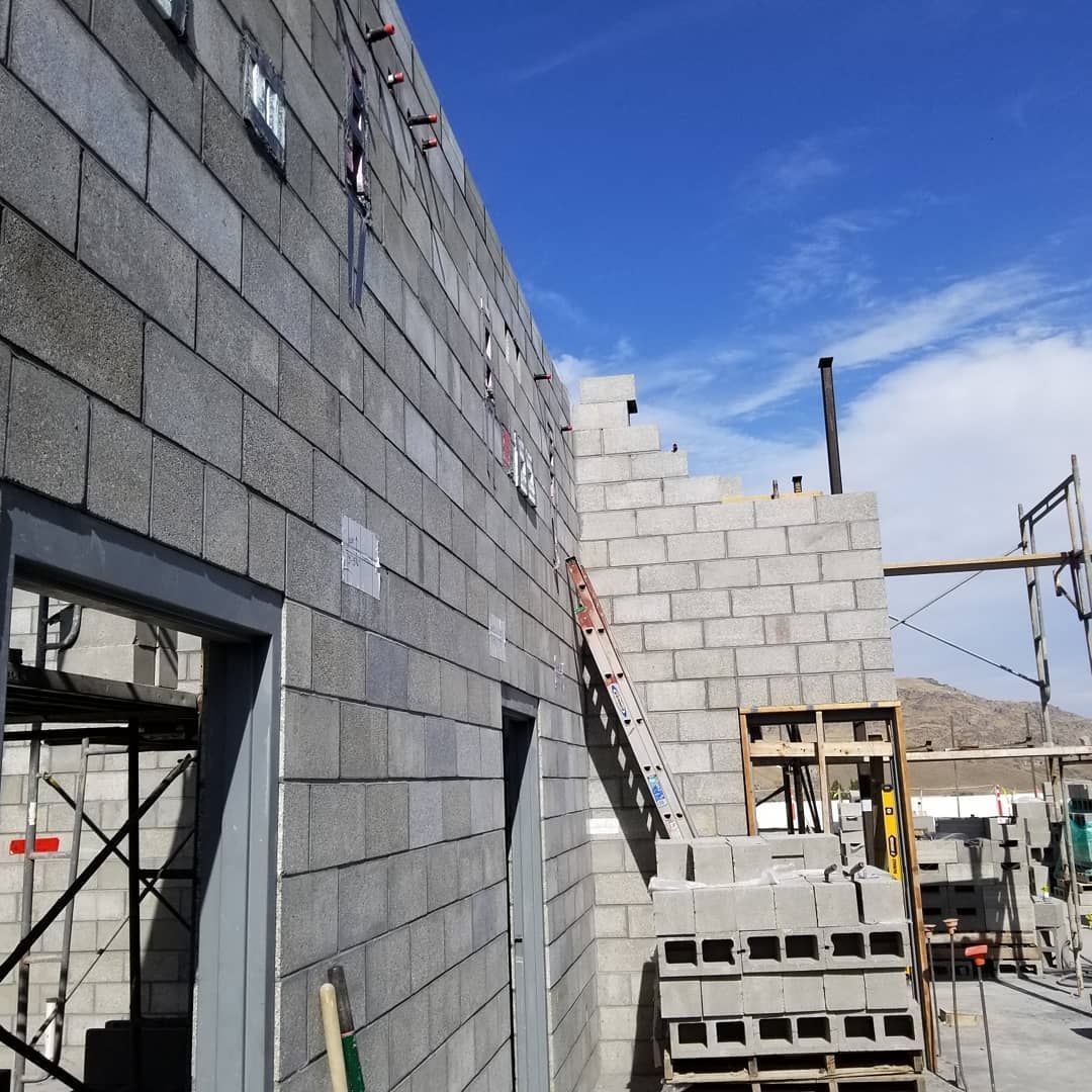 Building under construction, gray cinder block walls, scaffolding, blue sky.
