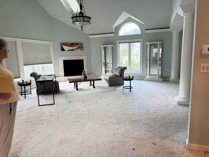 Woman surveys an empty living room with light blue walls, fireplace, and arched window.