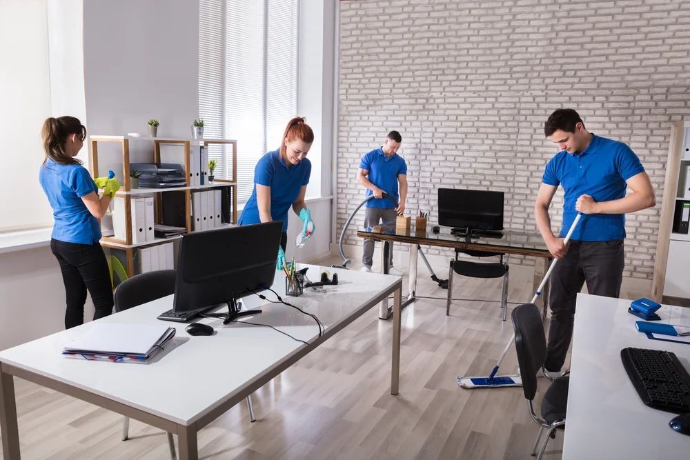 Office cleaners in blue shirts clean an office.