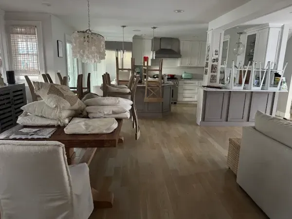 Bright, open-concept kitchen and dining area with wood floors, white walls, and a large wooden dining table.