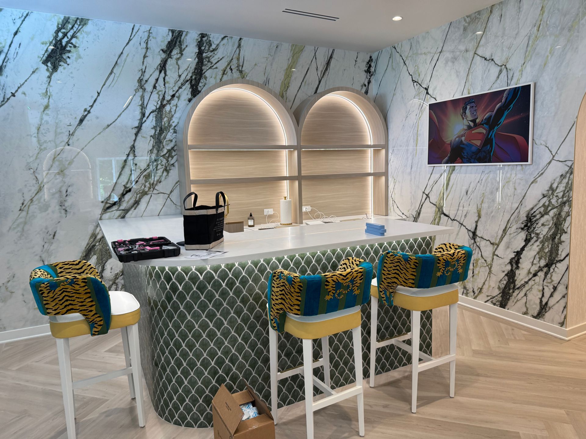 Lounge area with light wood floors, seating with tropical print, and a large plant art piece on the wall.