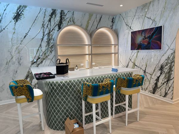 Lounge area with light wood floors, seating with tropical print, and a large plant art piece on the wall.