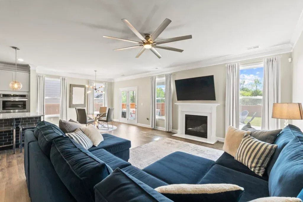 Spacious living room with blue sectional, fireplace, TV, and large windows.