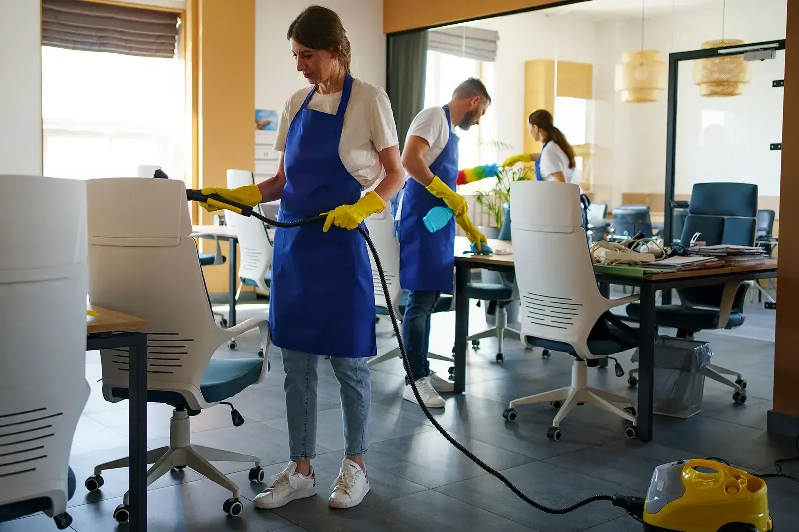 Office cleaners wearing blue aprons and yellow gloves steam cleaning chairs.