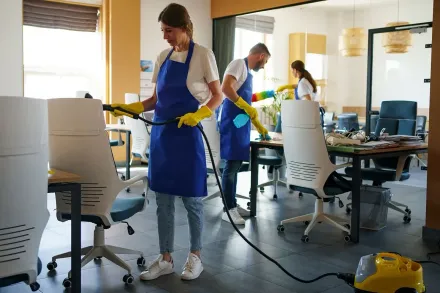 Office cleaners wearing blue aprons and yellow gloves steam cleaning chairs.