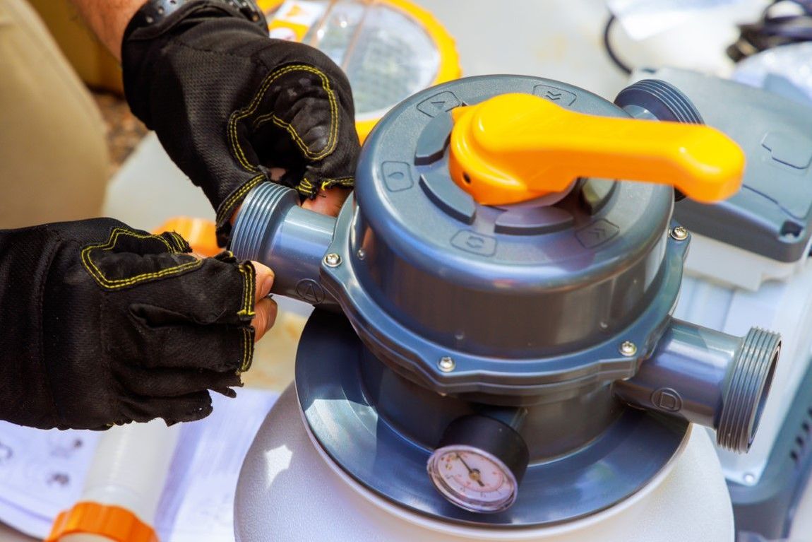 Person wearing black gloves connects a pool filter valve. The valve is grey with a yellow handle.