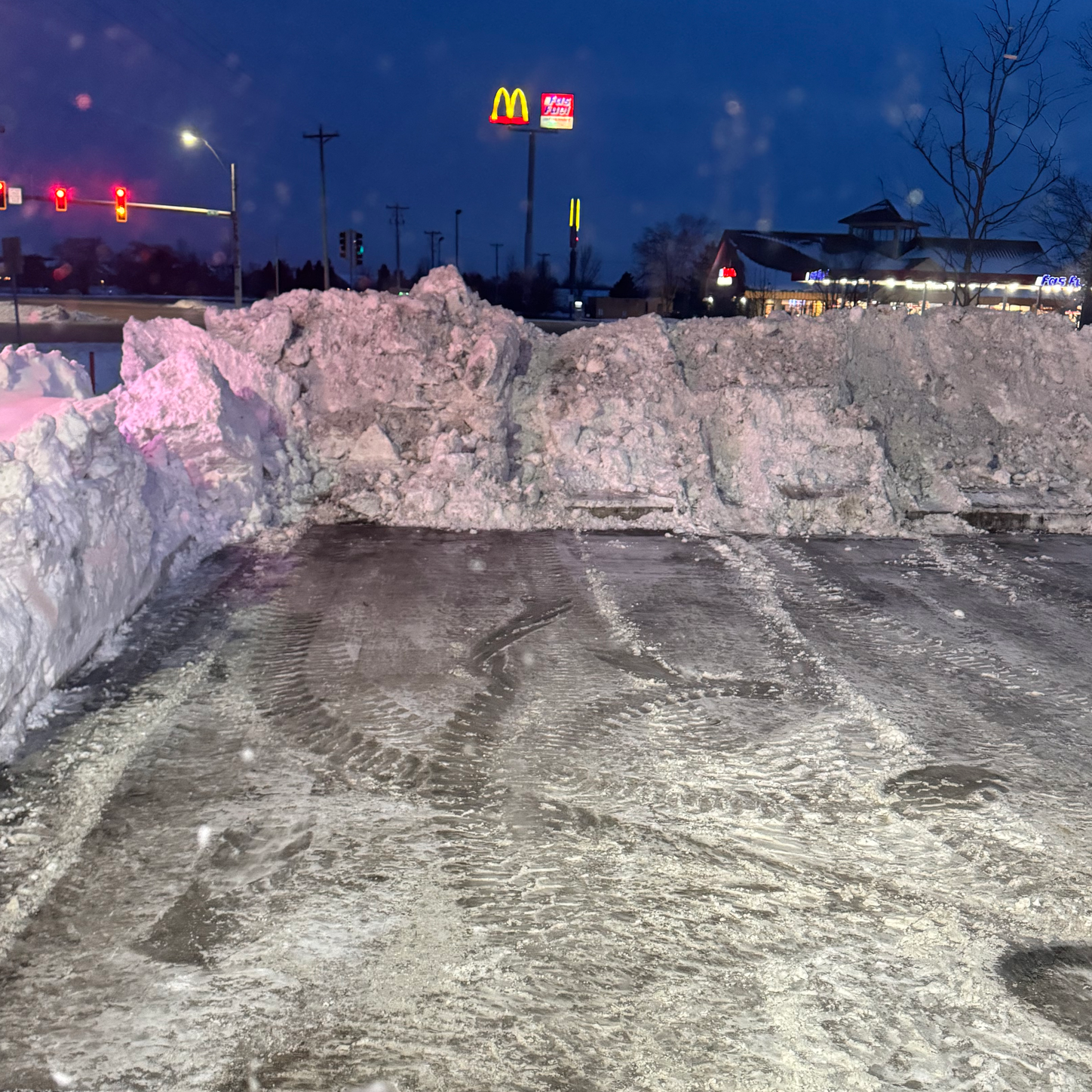 A large pile of snow in a parking lot with a mcdonald 's sign in the background