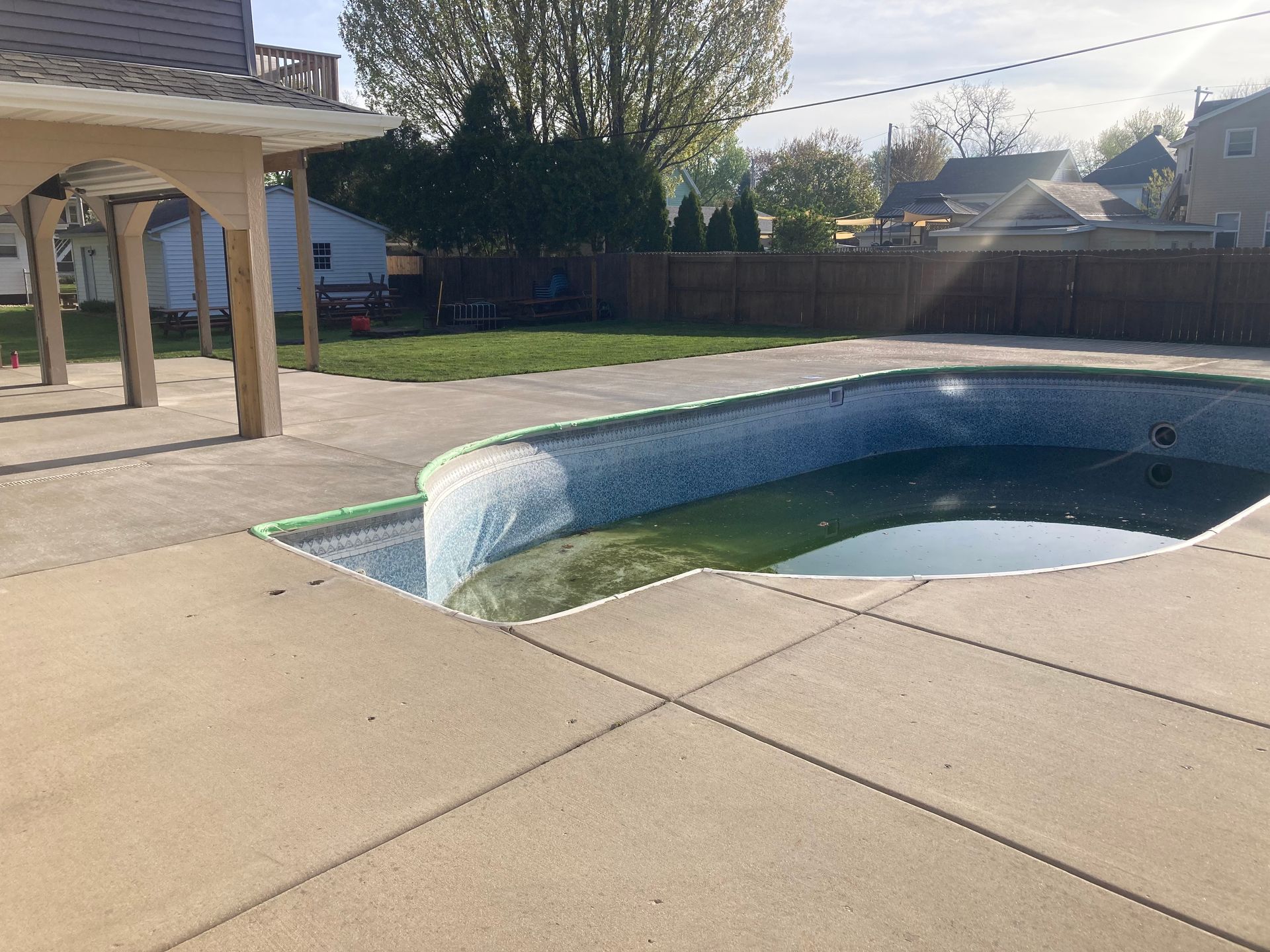 An empty swimming pool in a backyard with a house in the background