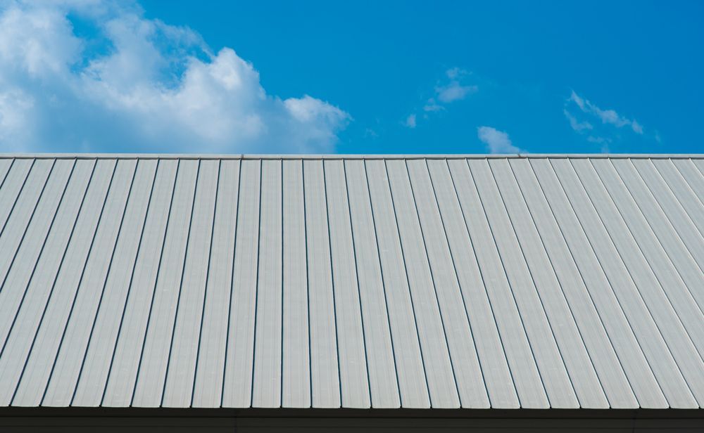 White metal roof against a bright blue sky with fluffy white clouds.