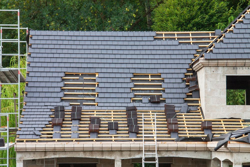 Roof under construction, partially covered with dark gray slate tiles, scaffolding present.