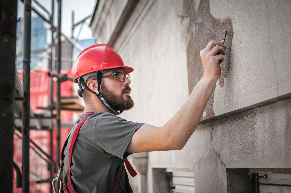 Construction worker in a red hard hat, using a tool on a building exterior.