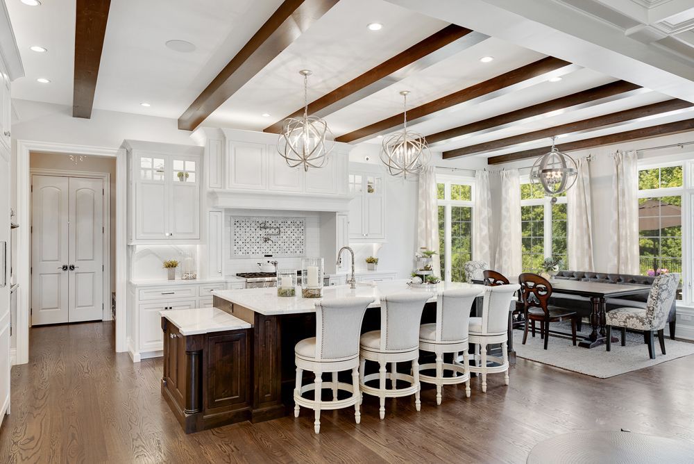Elegant white kitchen with dark island, wood beams, and dining area.