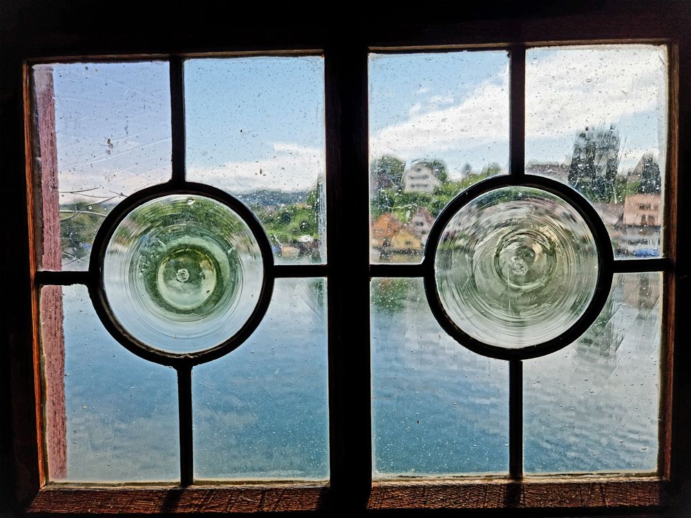 Two-pane window with circular glass panes overlooking a lake and buildings.