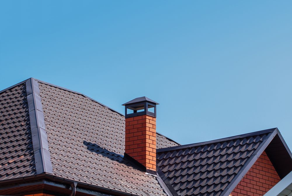 Brown shingle roof with a brick chimney against a blue sky.