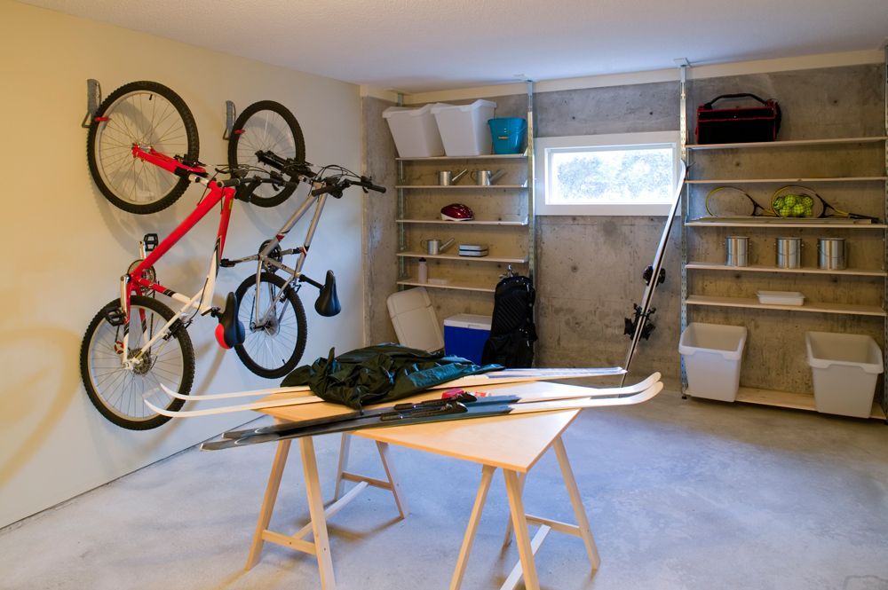 Garage storage: bikes, skis, and gear on shelves, a table with skis, against concrete walls.