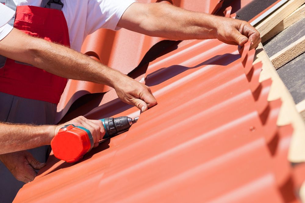Roofer installing red metal roofing with a drill.