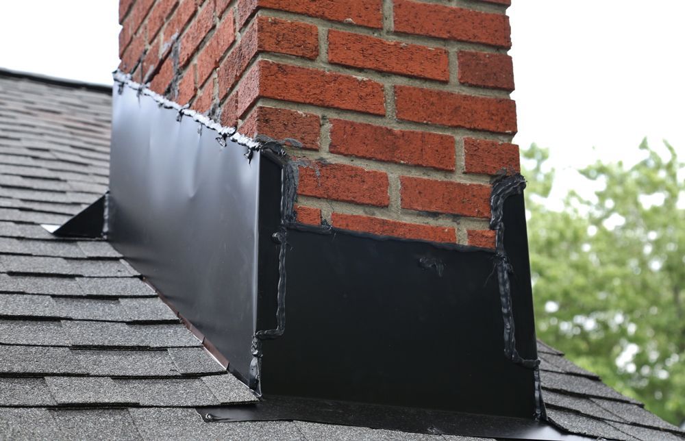 Brick chimney with black flashing on a shingled roof.