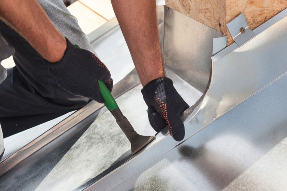Person wearing gloves uses a tool to shape metal flashing on a roof.