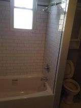 Bathroom with pink tub, white subway tile shower, toilet, and small window.