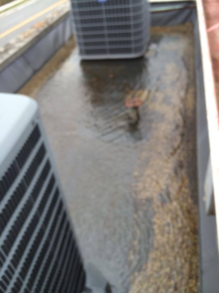 Water pooling on a flat roof, surrounding HVAC units and gravel, indicating a potential drainage issue.