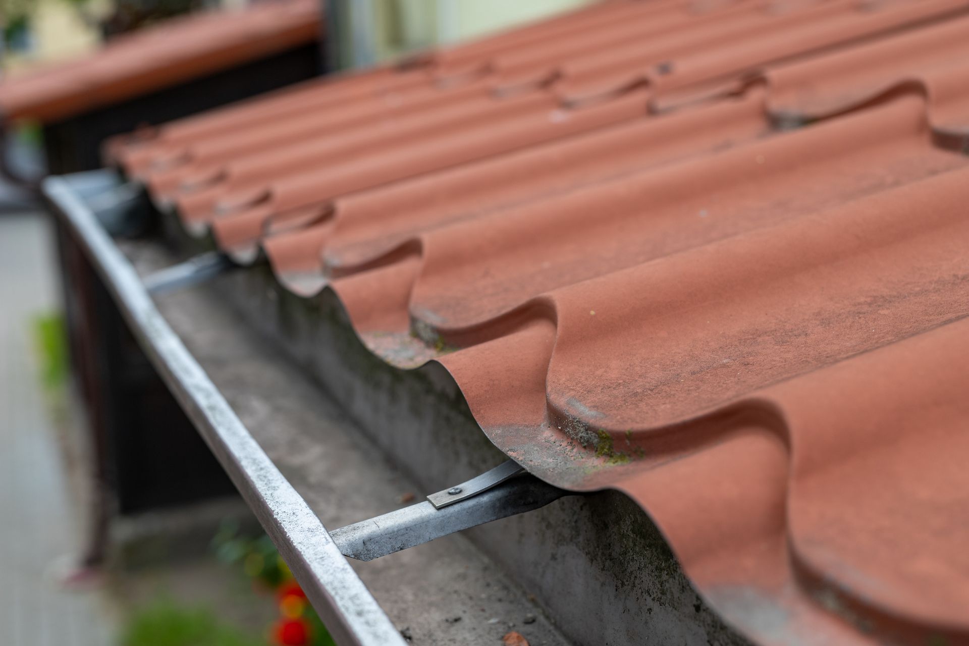 Close-up of red clay roof tiles with metal gutter brackets on residential roofing.