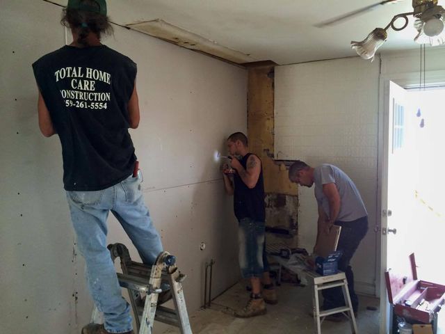 Three men working in a room undergoing renovation. One on a ladder, two near a beam, using tools.