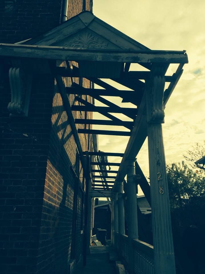 A covered walkway with support beams attached to a brick building and columns.
