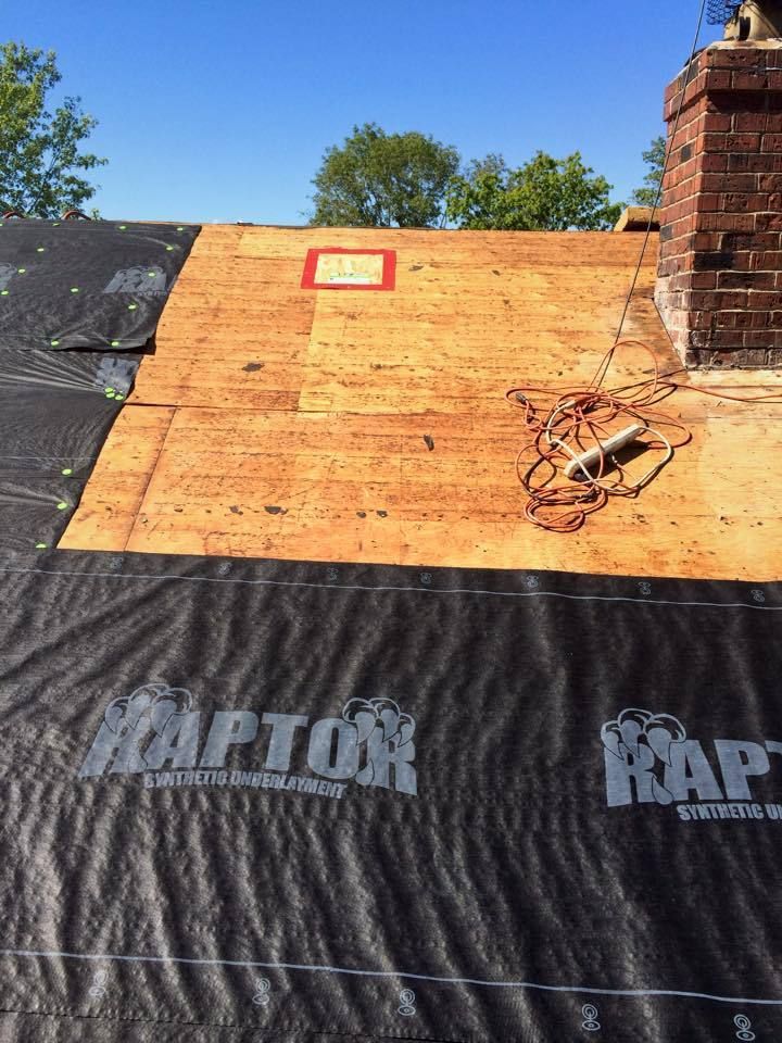 Roofing construction: black underlayment, exposed wooden boards, brick chimney, and coiled rope.