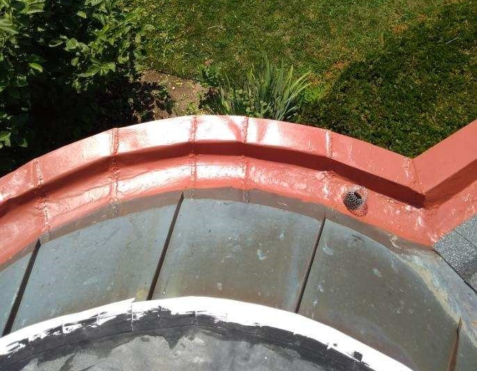 Close-up of a weathered, curved metal roof with red trim and a black drainage pipe, outdoors.