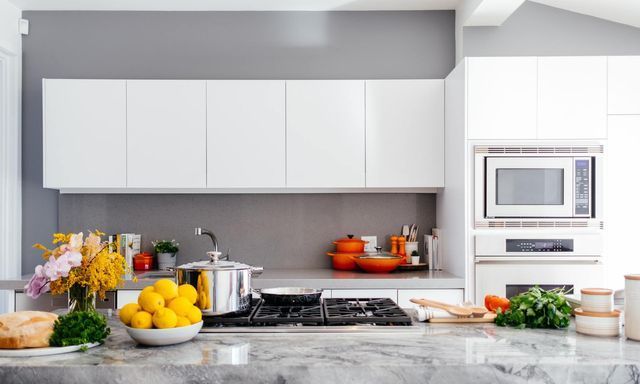 Modern white kitchen with gray walls, stainless steel appliances, and food on the counter.