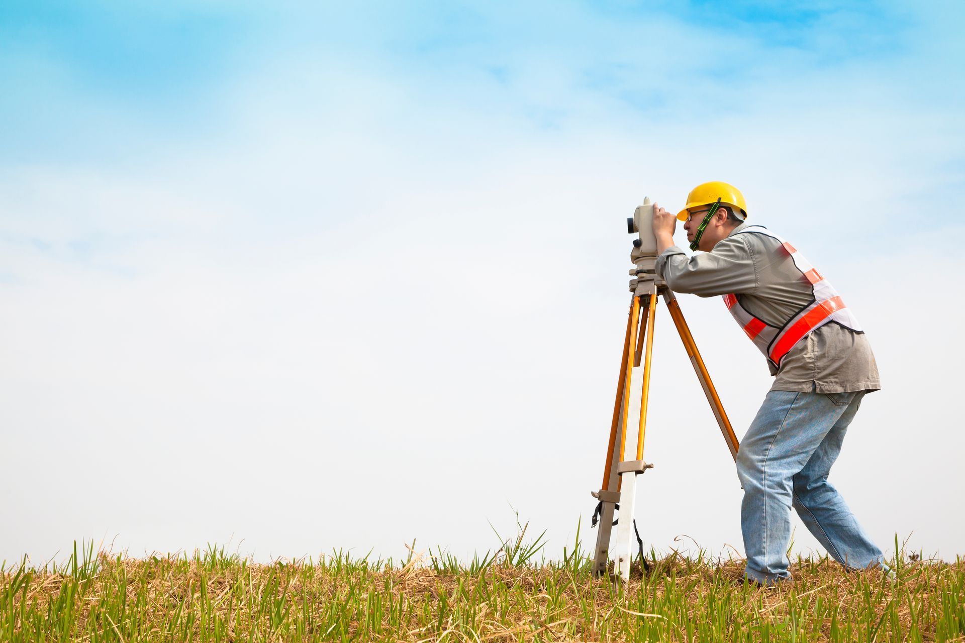 Surveyor uses a tripod-mounted level while working on open land under a clear sky. Surveyor uses a tripod-mounted level while working on open land under a clear sky.