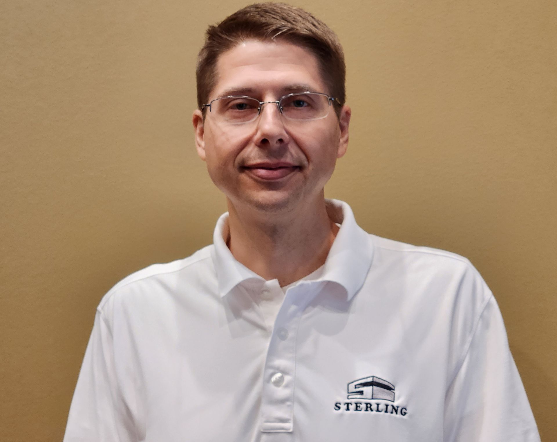 Man wearing glasses and a white polo shirt with the word