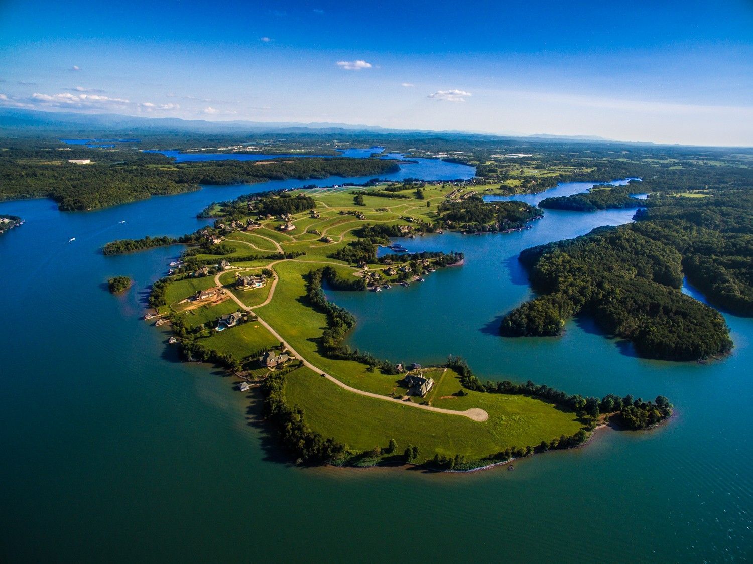 Aerial view of a lush green peninsula surrounded by a large body of blue water. Buildings and trees are visible.
