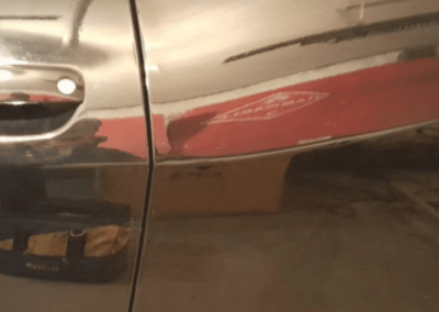 Black car door with a dent, reflecting a red object and garage interior.