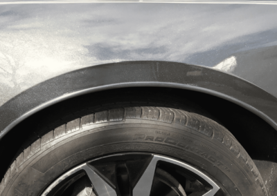 Close-up of a black car tire and wheel well with a curved black trim, set outdoors.