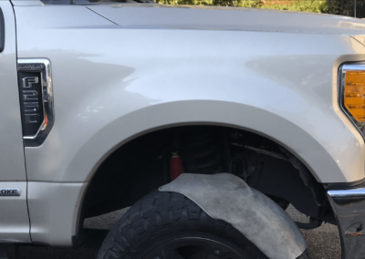 Tan pickup truck front wheel and fender, outdoor setting.