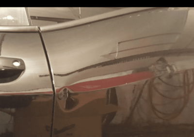 Damaged black car door with dent and red reflection.