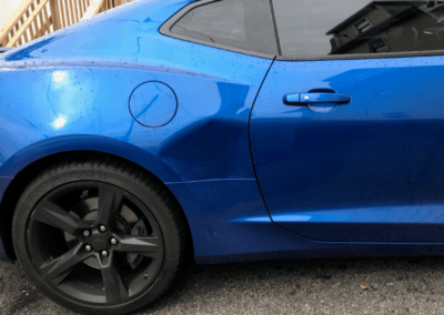 Blue sports car with black wheels, fuel door, and door handle visible.