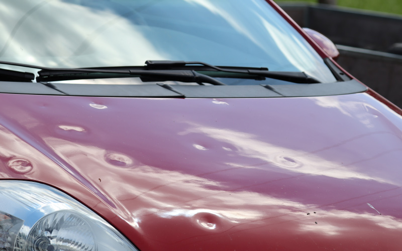 Red car hood dented from hail damage.
