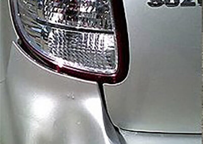 Silver car rear detail showing a taillight, a curved body panel, and the word 
