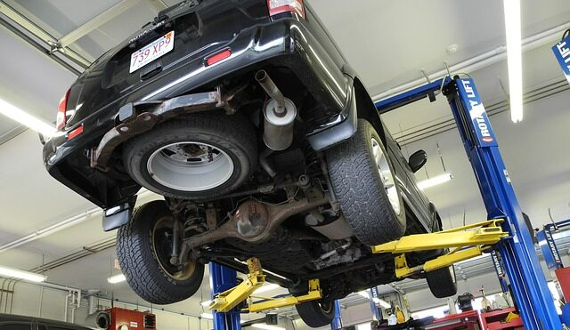 Black SUV on a hydraulic lift in a garage, undercarriage visible.