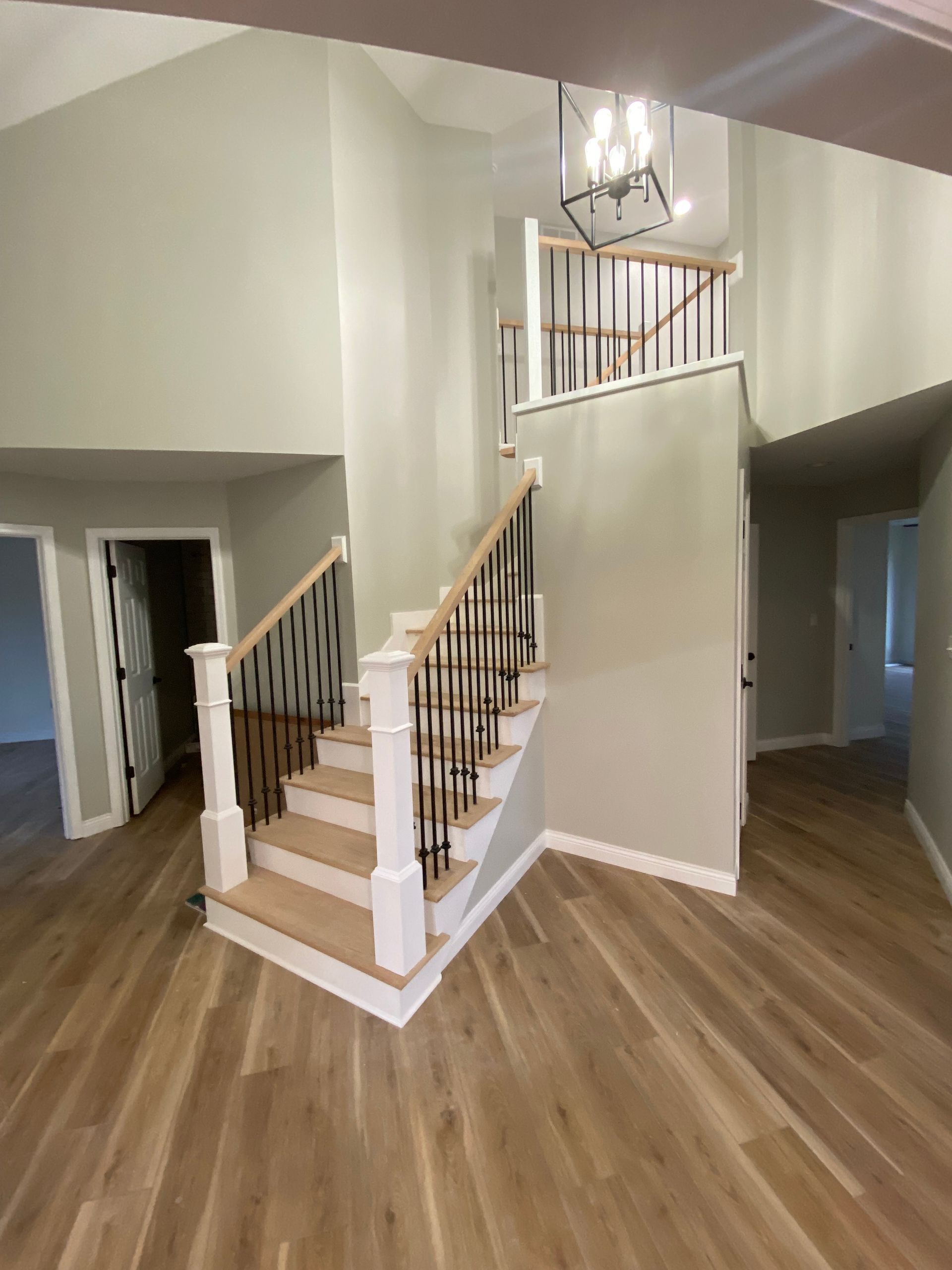 Interior view of a two-story foyer with a staircase. Light wood flooring, gray walls, and a black and white banister.