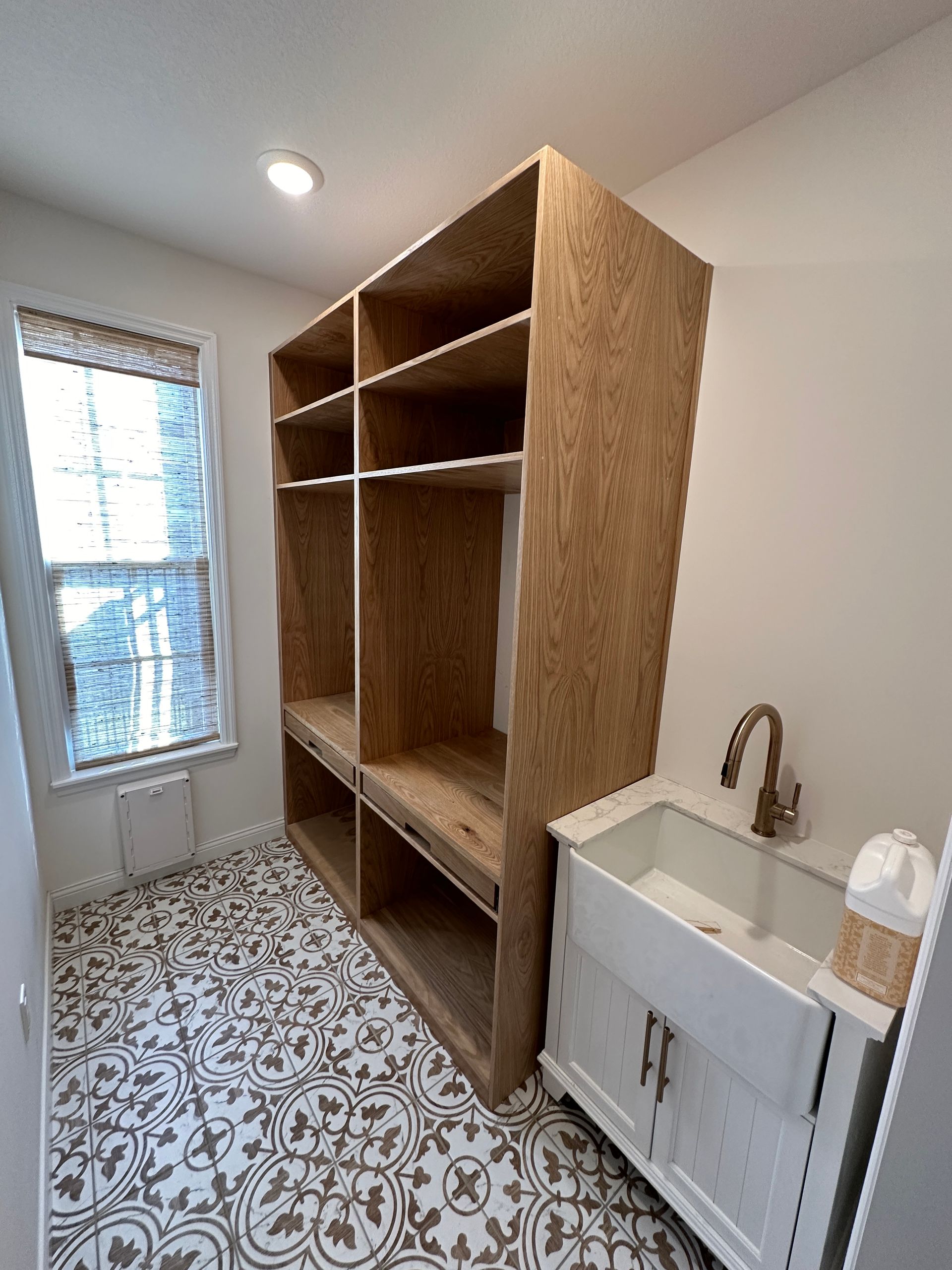Laundry room with open shelving, sink, window with blinds, and patterned tile floor.